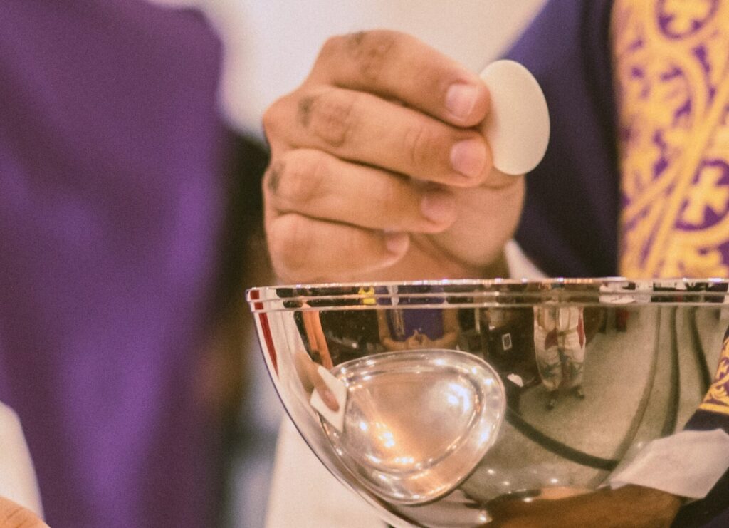 Priest's hand holding a wafer over a goblet of wine